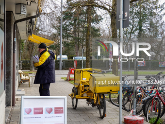 In Munich, Bavaria, Germany, on December 19, 2024, a Deutsche Post postman delivers letters to a residential building, with his yellow deliv...