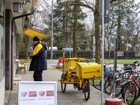 In Munich, Bavaria, Germany, on December 19, 2024, a Deutsche Post postman delivers letters to a residential building, with his yellow deliv...