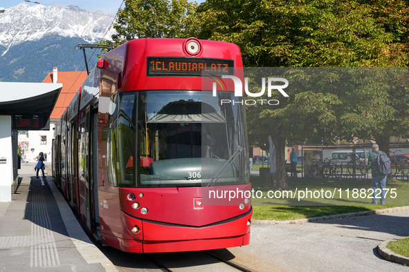 In Innsbruck, Austria, on September 22, 2024, a red tram bound for Claudiaplatz is at the Stift Wilten tram stop, against a backdrop of gree...