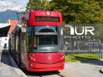 In Innsbruck, Austria, on September 22, 2024, a red tram bound for Claudiaplatz is at the Stift Wilten tram stop, against a backdrop of gree...