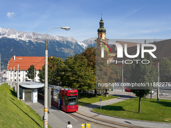 In Innsbruck, Austria, on September 22, 2024, a tram stops at Stift Wilten tram station, with the Wilten Basilica and the Tyrolean Alps in t...