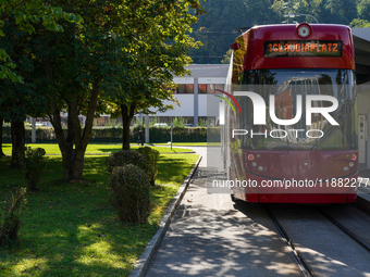 In Innsbruck, Austria, on September 22, 2024, a red tram heads to Claudiaplatz at the Stift Wilten tram stop, surrounded by greenery and ill...