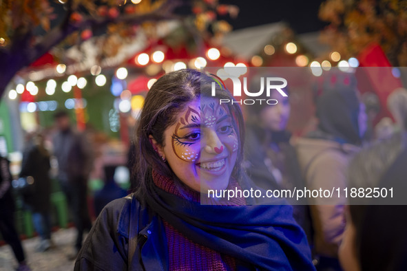 A young Iranian woman with a painting on her face smiles while participating in a pomegranate festival on Yalda Night Eve in the Abasabad to...