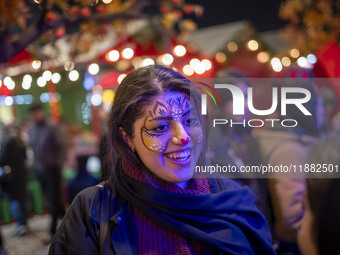 A young Iranian woman with a painting on her face smiles while participating in a pomegranate festival on Yalda Night Eve in the Abasabad to...