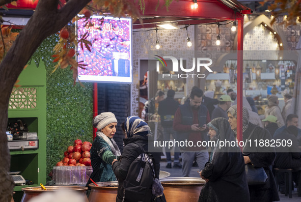 Iranian women shop for pomegranate molasses from a saleswoman while visiting a pomegranate festival on Yalda Night Eve in the Abasabad touri...