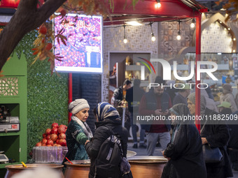 Iranian women shop for pomegranate molasses from a saleswoman while visiting a pomegranate festival on Yalda Night Eve in the Abasabad touri...