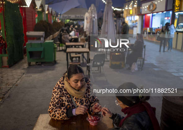 Two young women eat Iranian traditional pomegranate dessert while visiting a pomegranate festival on Yalda Night Eve in the Abasabad tourism...