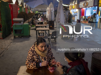 Two young women eat Iranian traditional pomegranate dessert while visiting a pomegranate festival on Yalda Night Eve in the Abasabad tourism...