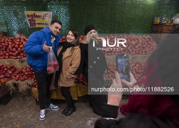 Iranian youths pose for a photograph as one of them carries pomegranates in a plastic bag while shopping for the Yalda Night ceremony during...