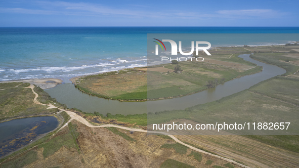 An aerial view shows the Ofanto River meeting the Adriatic Sea, highlighting the contrast between the green riverbanks and the blue sea in P...