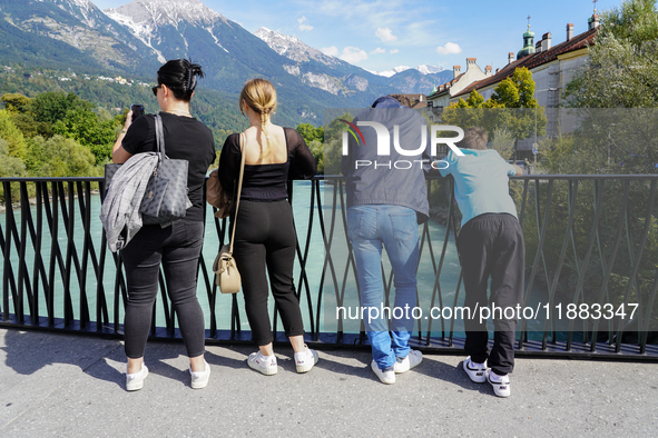 A group of people stands on a bridge overlooking the turquoise waters of the Inn River in Innsbruck, Austria, on September 22, 2024, with th...