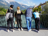 A group of people stands on a bridge overlooking the turquoise waters of the Inn River in Innsbruck, Austria, on September 22, 2024, with th...