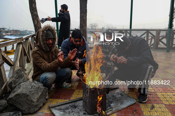 People warm themselves by a bonfire on a cold winter morning at Dal Lake in Srinagar, Jammu and Kashmir, India, on December 20, 2024. Srinag...