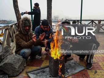 People warm themselves by a bonfire on a cold winter morning at Dal Lake in Srinagar, Jammu and Kashmir, India, on December 20, 2024. Srinag...