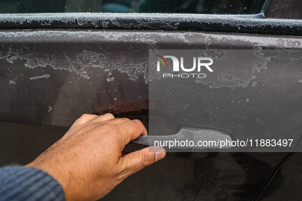 A person tries to open a frosted car door on a cold day in Srinagar, Jammu and Kashmir, India, on December 20, 2024. 