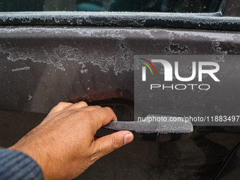 A person tries to open a frosted car door on a cold day in Srinagar, Jammu and Kashmir, India, on December 20, 2024. (