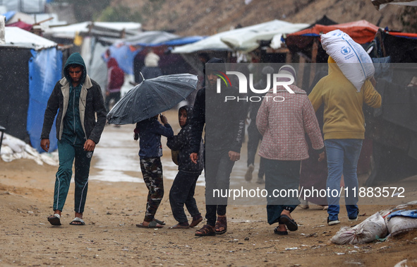 Displaced Palestinians walk in the rain at a makeshift camp in Khan Yunis, Gaza Strip, on December 20, 2024, amid the ongoing war between Is...