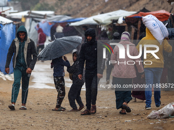 Displaced Palestinians walk in the rain at a makeshift camp in Khan Yunis, Gaza Strip, on December 20, 2024, amid the ongoing war between Is...