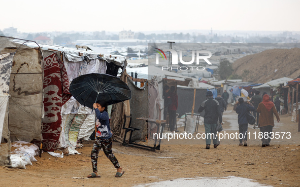 A Palestinian girl carries an umbrella to fend off the rain at a makeshift camp in Khan Yunis, Gaza Strip, on December 20, 2024, amid the on...