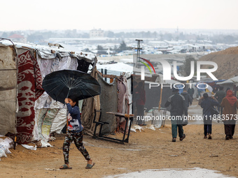 A Palestinian girl carries an umbrella to fend off the rain at a makeshift camp in Khan Yunis, Gaza Strip, on December 20, 2024, amid the on...