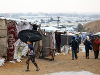 A Palestinian girl carries an umbrella to fend off the rain at a makeshift camp in Khan Yunis, Gaza Strip, on December 20, 2024, amid the on...