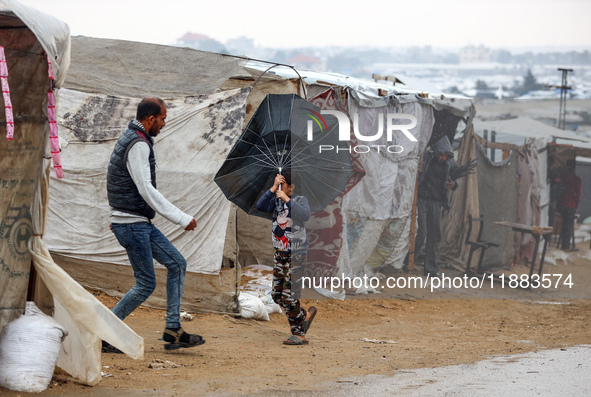 A Palestinian girl carries an umbrella to fend off the rain at a makeshift camp in Khan Yunis, Gaza Strip, on December 20, 2024, amid the on...