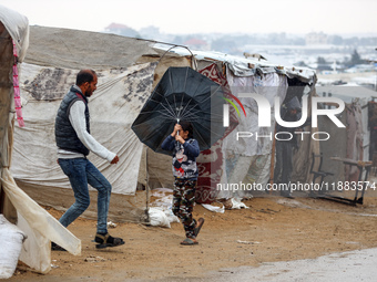 A Palestinian girl carries an umbrella to fend off the rain at a makeshift camp in Khan Yunis, Gaza Strip, on December 20, 2024, amid the on...