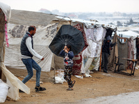 A Palestinian girl carries an umbrella to fend off the rain at a makeshift camp in Khan Yunis, Gaza Strip, on December 20, 2024, amid the on...