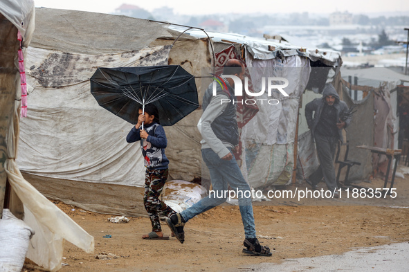 Displaced Palestinians walk in the rain at a makeshift camp in Khan Yunis, Gaza Strip, on December 20, 2024, amid the ongoing war between Is...