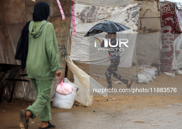 A Palestinian girl carries an umbrella to fend off the rain at a makeshift camp in Khan Yunis, Gaza Strip, on December 20, 2024, amid the on...