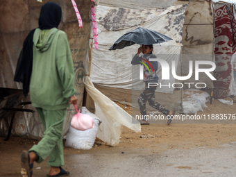 A Palestinian girl carries an umbrella to fend off the rain at a makeshift camp in Khan Yunis, Gaza Strip, on December 20, 2024, amid the on...