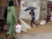 A Palestinian girl carries an umbrella to fend off the rain at a makeshift camp in Khan Yunis, Gaza Strip, on December 20, 2024, amid the on...