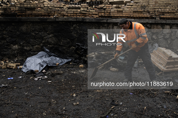 Communal workers clean the street as the body of a person killed in a Russian missile strike lies nearby in central Kyiv, Ukraine, on Decemb...