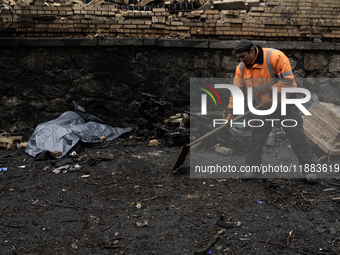 Communal workers clean the street as the body of a person killed in a Russian missile strike lies nearby in central Kyiv, Ukraine, on Decemb...