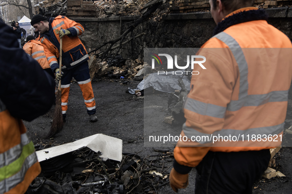 Communal workers clean the street as the body of a person killed in a Russian missile strike lies nearby in central Kyiv, Ukraine, on Decemb...