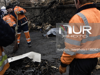 Communal workers clean the street as the body of a person killed in a Russian missile strike lies nearby in central Kyiv, Ukraine, on Decemb...