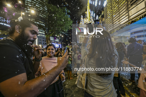 Visitors celebrate after artificial snow fills the Christmas decoration outside a shopping mall in Kuala Lumpur, Malaysia, on December 19, 2...