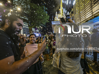 Visitors celebrate after artificial snow fills the Christmas decoration outside a shopping mall in Kuala Lumpur, Malaysia, on December 19, 2...