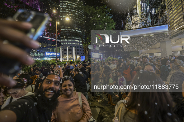 Visitors celebrate after artificial snow fills the Christmas decoration outside a shopping mall in Kuala Lumpur, Malaysia, on December 19, 2...