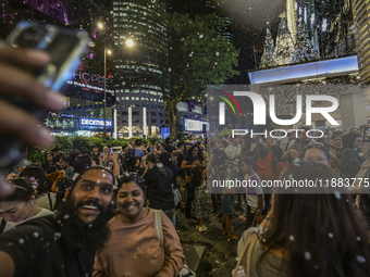 Visitors celebrate after artificial snow fills the Christmas decoration outside a shopping mall in Kuala Lumpur, Malaysia, on December 19, 2...