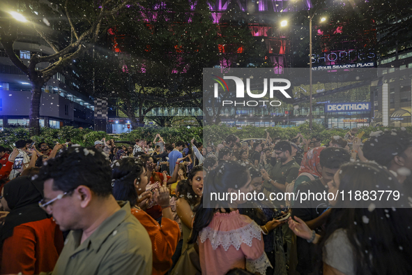 Visitors celebrate after artificial snow fills the Christmas decoration outside a shopping mall in Kuala Lumpur, Malaysia, on December 19, 2...