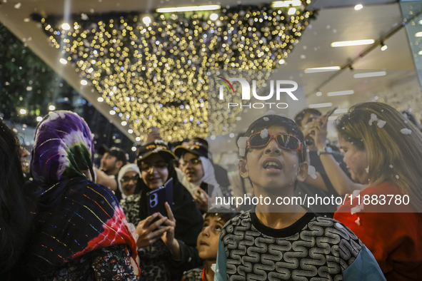 Visitors celebrate after artificial snow fills the Christmas decoration outside a shopping mall in Kuala Lumpur, Malaysia, on December 19, 2...