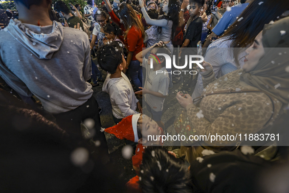 Visitors celebrate after artificial snow fills the Christmas decoration outside a shopping mall in Kuala Lumpur, Malaysia, on December 19, 2...