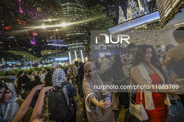 Visitors celebrate after artificial snow fills the Christmas decoration outside a shopping mall in Kuala Lumpur, Malaysia, on December 19, 2...