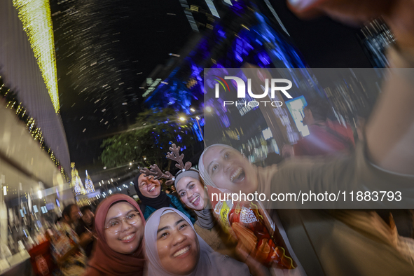 Visitors celebrate after artificial snow fills the Christmas decoration outside a shopping mall in Kuala Lumpur, Malaysia, on December 19, 2...