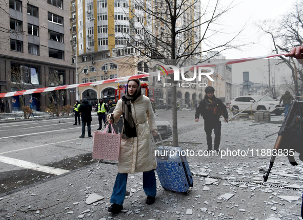 A woman pulls a suitcase along the street in the Holosiivskyi district covered with debris after a Russian missile attack in Kyiv, Ukraine,...