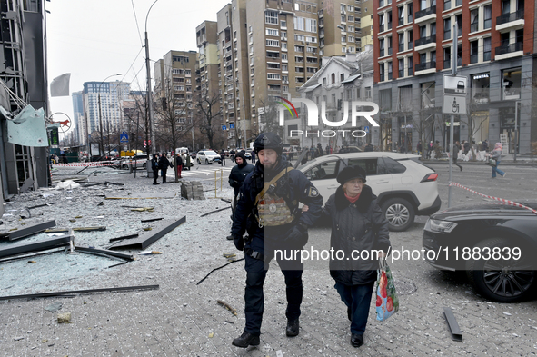 A police officer escorts an elderly woman in the street in the Holosiivskyi district damaged by a Russian missile attack in Kyiv, Ukraine, o...