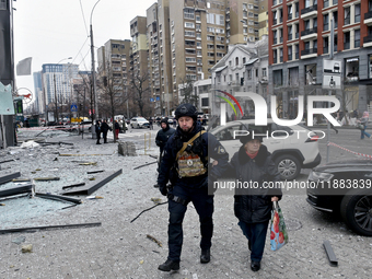 A police officer escorts an elderly woman in the street in the Holosiivskyi district damaged by a Russian missile attack in Kyiv, Ukraine, o...