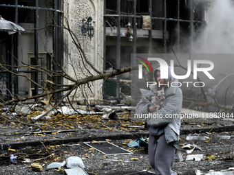 A woman carries a dog along a street covered with debris in the Holosiivskyi district after a Russian missile attack in Kyiv, Ukraine, on De...