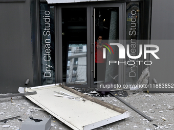 A woman stands at the smashed glass door of a dry cleaner in the Holosiivskyi district, damaged by a Russian missile attack, in Kyiv, Ukrain...